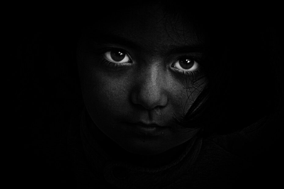 Das Bild vermittelt eindringlich die Emotionen und das Leid, das mit der Geschichte des Napalm-Mädchens Phan Thị Kim Phúc verbunden ist. Die dunkle, kontrastreiche Darstellung verstärkt das Gefühl von Schmerz, Angst und Hoffnungslosigkeit, das sie und viele andere Kinder im Vietnamkrieg erlebten. Die großen, leuchtenden Augen ziehen den Betrachter in ihren Bann und spiegeln den Schock, die Verletzlichkeit und die unaussprechliche Tragödie wider, die durch den Napalm-Angriff verursacht wurde. Die visuelle Inszenierung erinnert an das ikonische Foto von Phan Thị Kim Phúc, das die Schrecken des Krieges weltweit bekannt machte. Die Dunkelheit symbolisiert die Zerstörung und den Schrecken des Moments, während die Augen als einzig helle Elemente im Bild den Fokus auf das Trauma und die Unschuld des Kindes lenken. Diese Darstellung transportiert die emotionale Wucht der Geschichte, macht das Grauen spürbar und mahnt an die Folgen von Krieg und Gewalt.